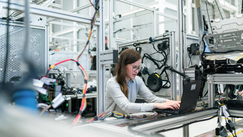 En kvindelig ingeniør der sidder og arbejder på en computer i et stort teknologirum